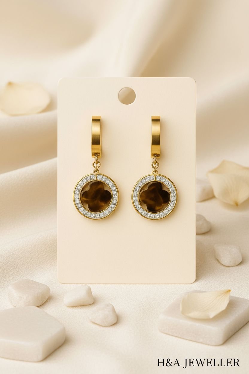 “Elegant gold drop earrings with circular crystal accents and dark brown floral center design, displayed on a cream card with luxury background — H&A Jeweller collection.”